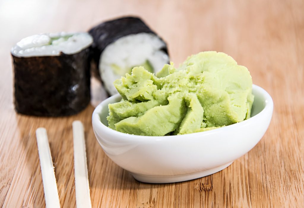 wasabi in a ceramic bowl, next to two pieces of sushi and a pair of chopsticks