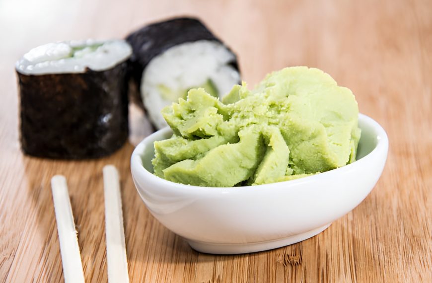 wasabi in a ceramic bowl, next to two pieces of sushi and a pair of chopsticks